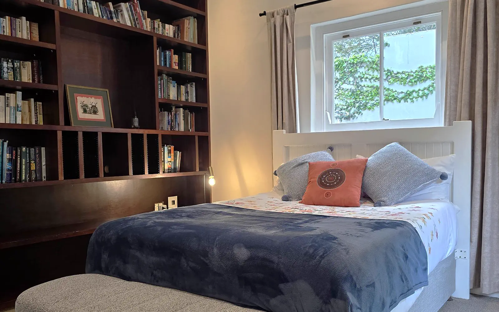 The Library: a wall-to-wall dark wood bookcase beside the made bed, with a window onto the garden