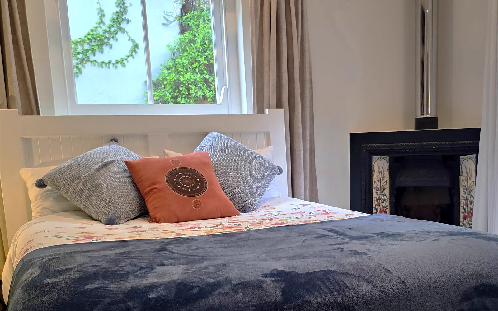 The Library bed with cushions, a wood-burning stove and daylight through the windows