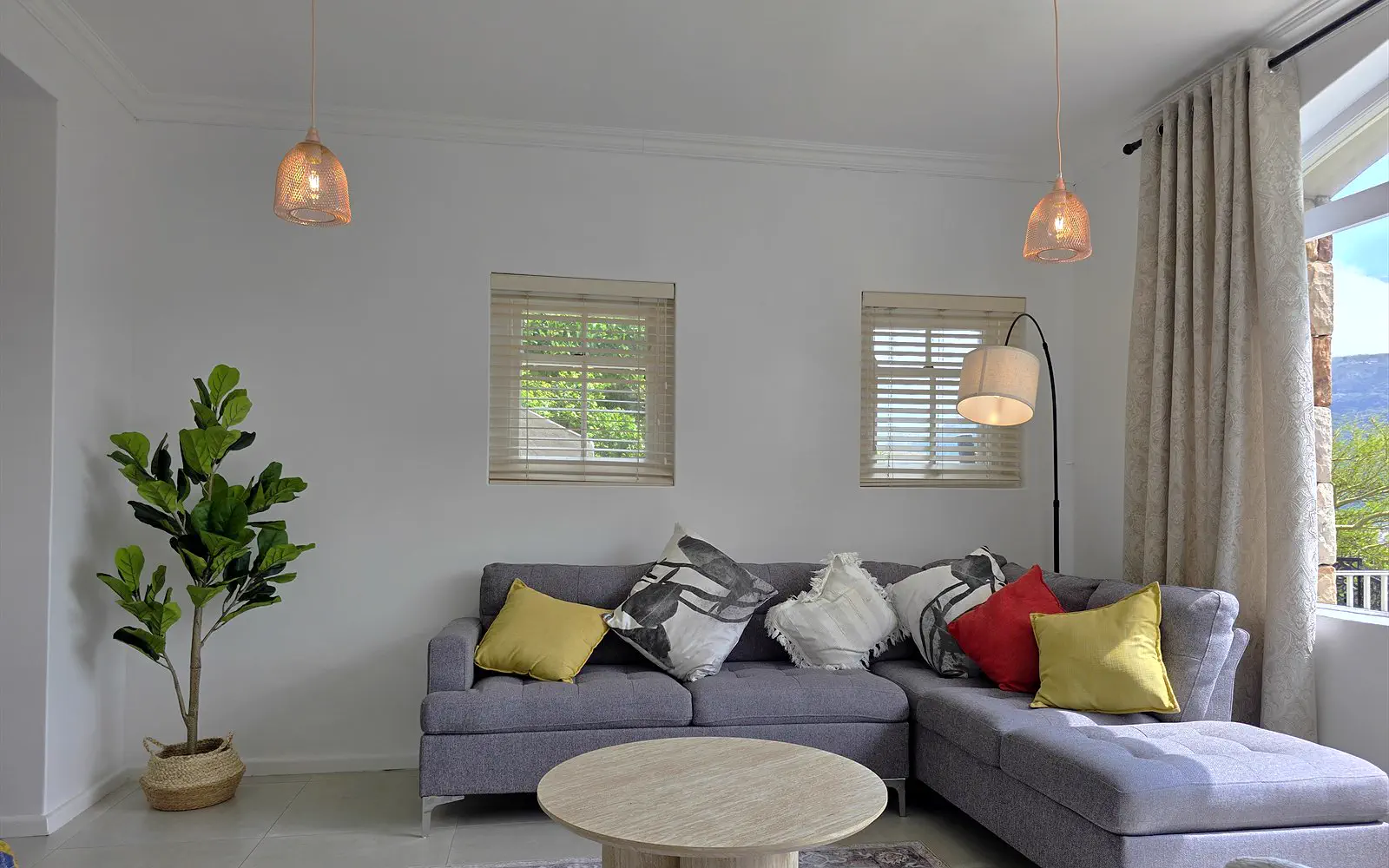 Seating area of The Lodge with grey corner sofa, coffee table, fig tree and pendant lights