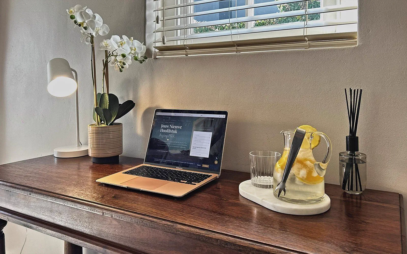 Antique wooden desk with laptop, orchid and a carafe of lemon water