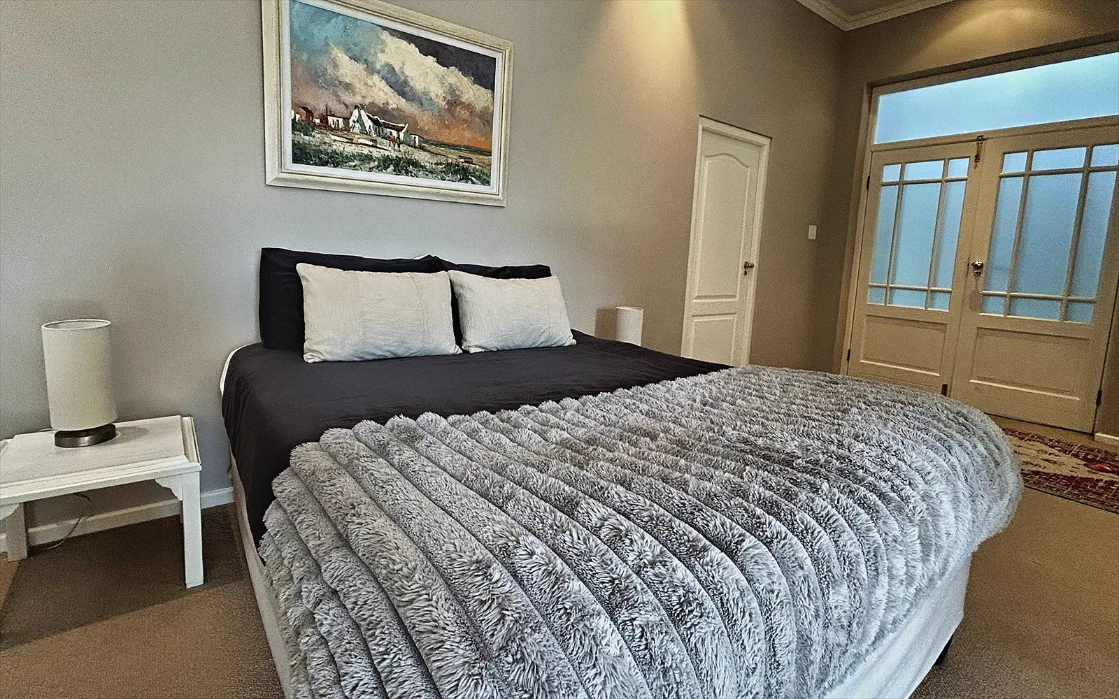 Made bed with a soft throw and French doors to the outside