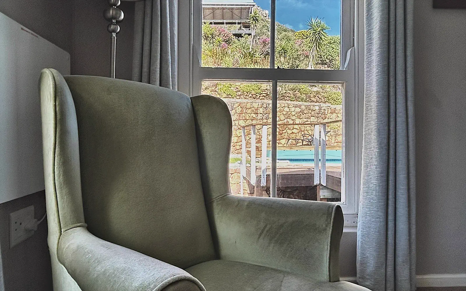 Green wingback chair by the window with a view of the pool and the hill