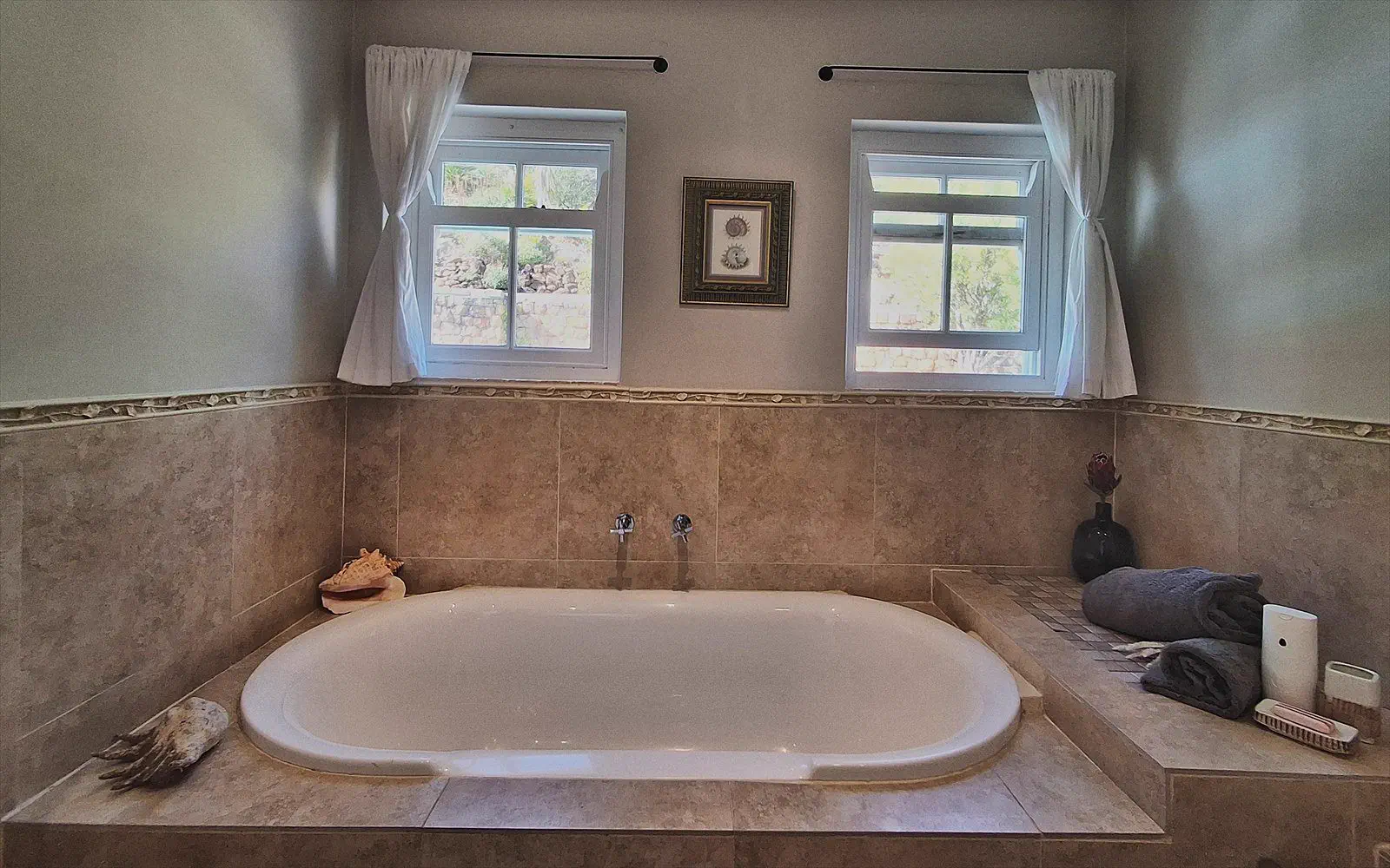 The private bathroom of The Split with a bath beneath two windows and travertine tiles