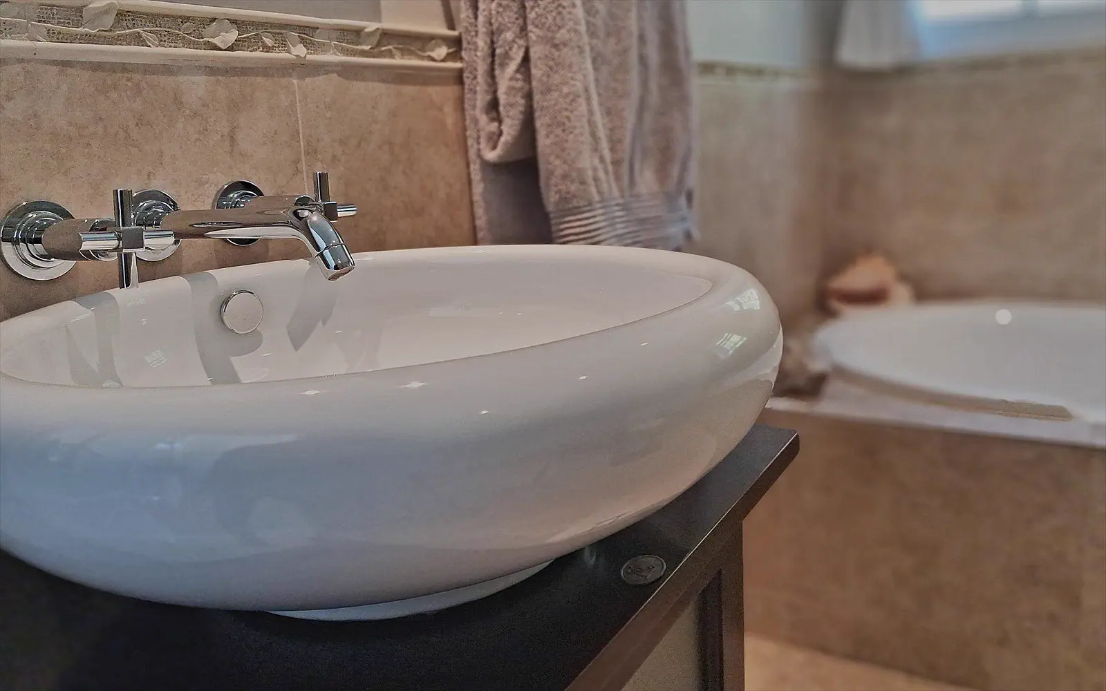 Freestanding basin with wall taps, towels and the bath in the background