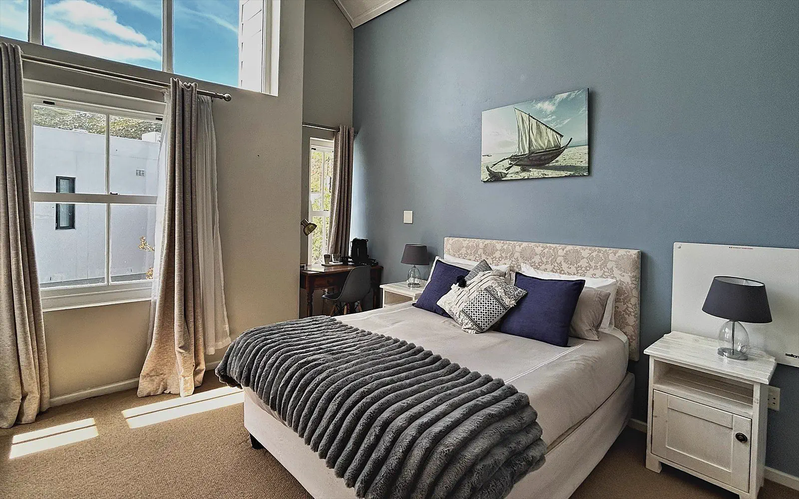 The Suite bedroom with a light blue wall, tall window and its own desk